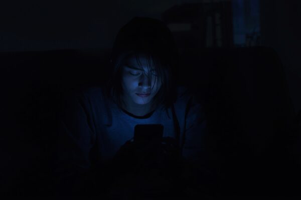Person sitting alone in dimly lit room illuminated by phone screen glow, symbolizing AI chatbot emotional support