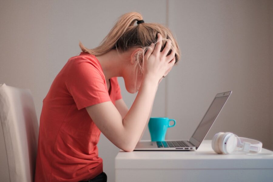 Stressed young woman at a kitchen table with a laptop and coffee, feeling she never has enough time