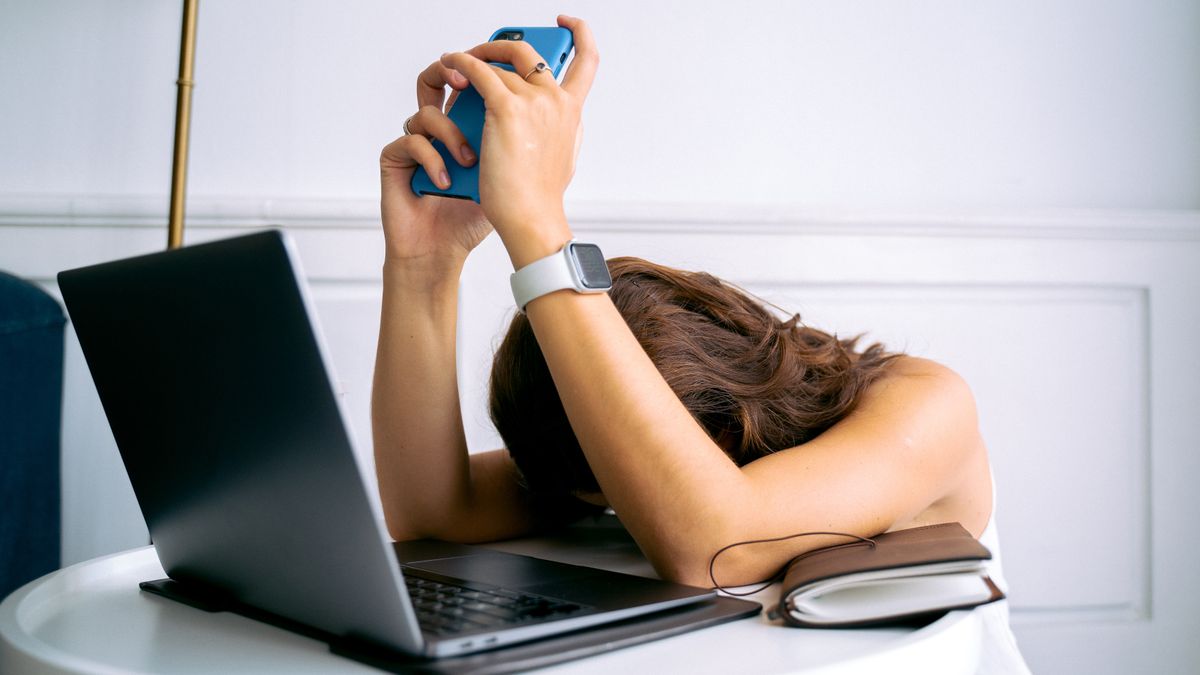 A person sitting at a kitchen table in soft morning light with coffee and an open laptop, looking quietly overwhelmed by the day ahead