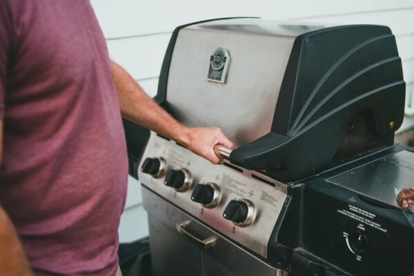 Hands slowly opening a propane tank valve to reset a gas grill regulator stuck in bypass mode